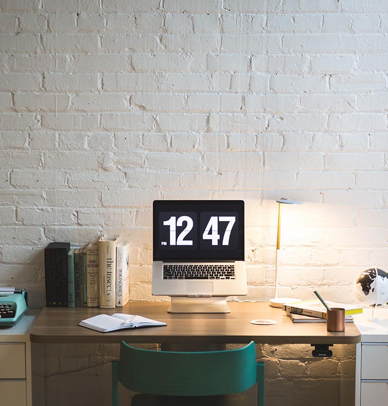 Minimalist workspace with a computer displaying time, books, a notebook, and a desk lamp, reflecting an organized environment suitable for productivity and industrial insights.